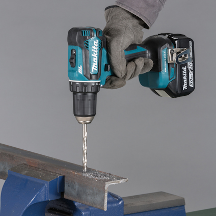 En person borrar ett metallstycke med en blå Makita-borrmaskin i ett skruvstäd.